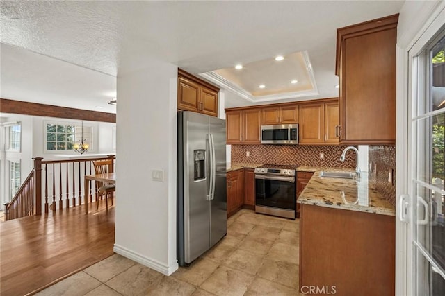 kitchen featuring light stone countertops, a wealth of natural light, appliances with stainless steel finishes, sink, and a raised ceiling