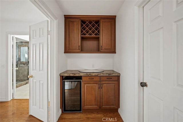 bar featuring wine cooler, stone countertops, and light hardwood / wood-style floors