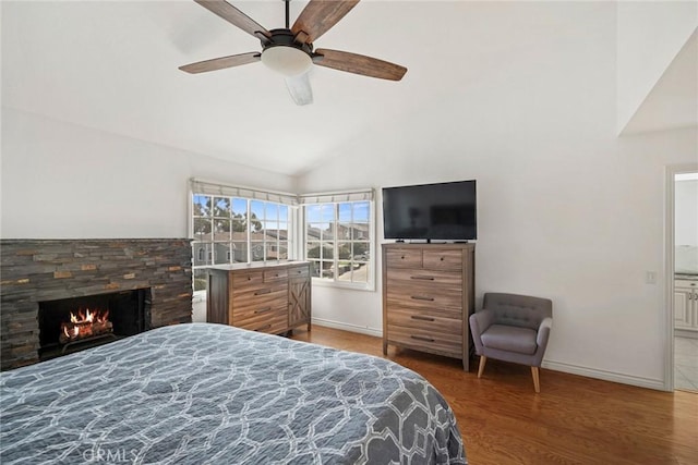 bedroom with ceiling fan, wood-type flooring, a stone fireplace, and vaulted ceiling