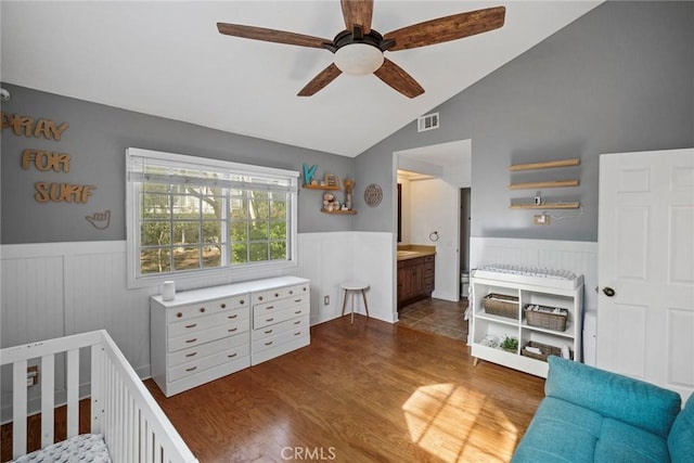 bedroom featuring lofted ceiling, dark wood-type flooring, a crib, ceiling fan, and ensuite bathroom