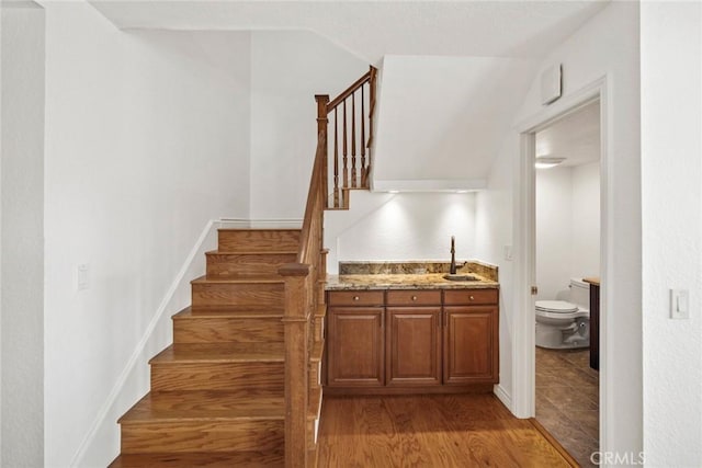 stairs with lofted ceiling, wood-type flooring, and sink