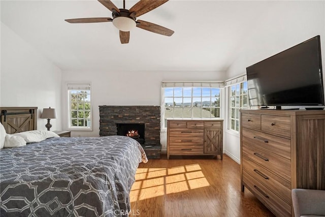 bedroom featuring vaulted ceiling, ceiling fan, a fireplace, and hardwood / wood-style floors