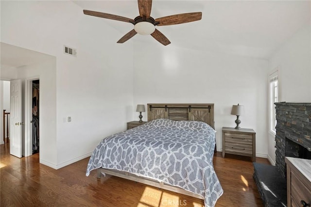 bedroom featuring a spacious closet, ceiling fan, a closet, dark wood-type flooring, and a fireplace