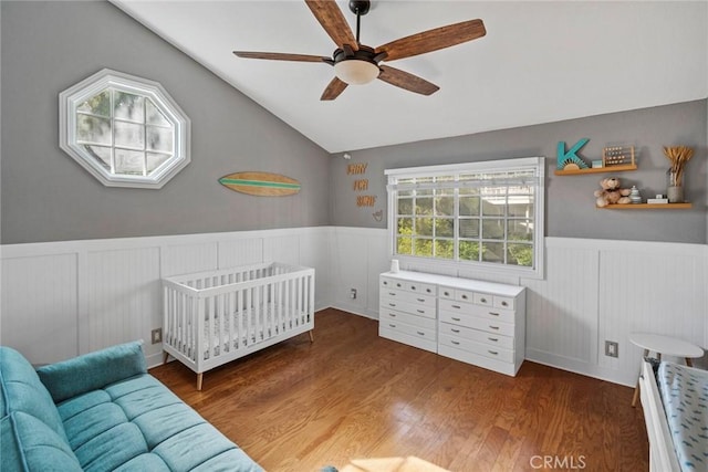 bedroom with ceiling fan, lofted ceiling, wood-type flooring, and a crib