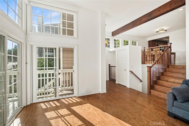 interior space with beam ceiling, a high ceiling, and hardwood / wood-style floors