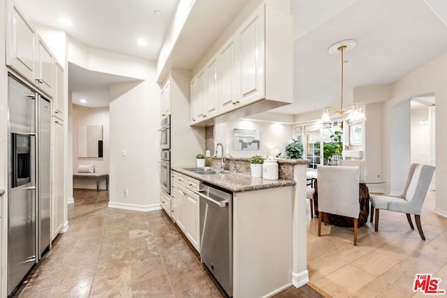 kitchen with sink, hanging light fixtures, appliances with stainless steel finishes, white cabinets, and light stone counters