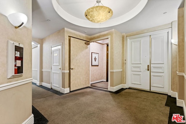 interior space with a tray ceiling and dark colored carpet