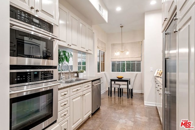 kitchen featuring decorative light fixtures, sink, white cabinetry, and appliances with stainless steel finishes