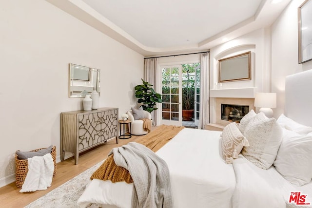 bedroom with light hardwood / wood-style floors, a tray ceiling, and access to outside