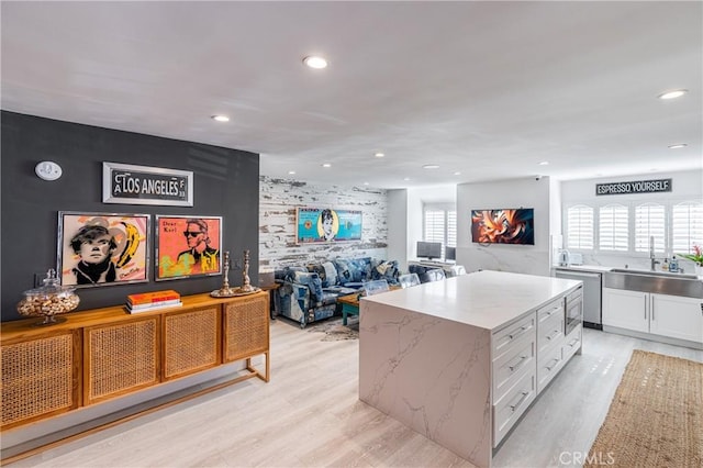 kitchen featuring light hardwood / wood-style floors, dishwasher, a kitchen island, white cabinets, and sink