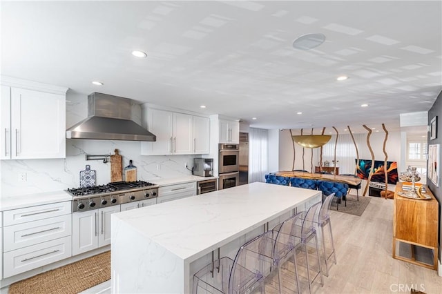 kitchen with white cabinets, wall chimney exhaust hood, stainless steel appliances, decorative backsplash, and light wood-type flooring