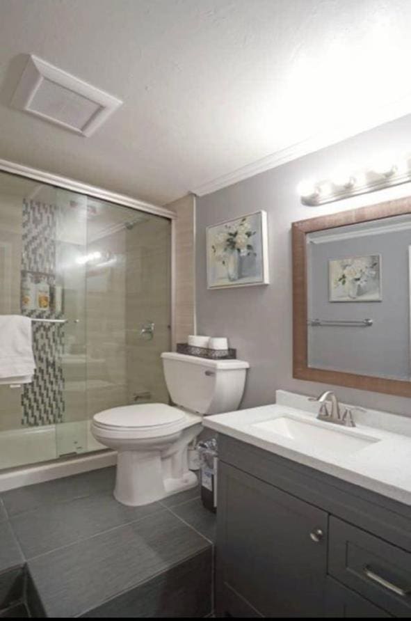 bathroom featuring tile patterned floors, toilet, a shower with shower door, and vanity