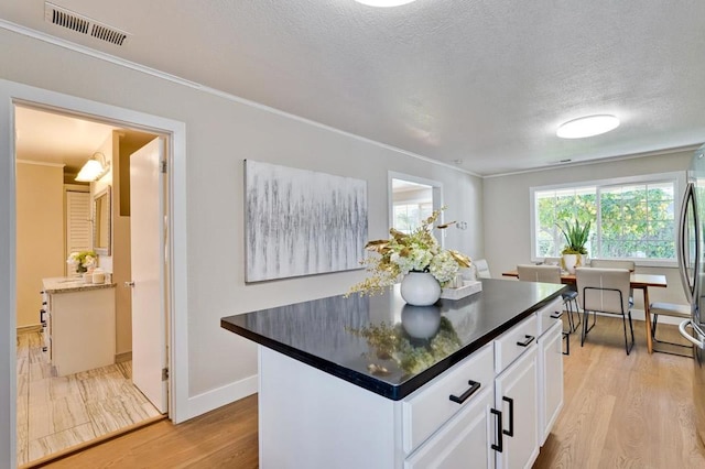 kitchen with white cabinetry, ornamental molding, light hardwood / wood-style floors, and a textured ceiling