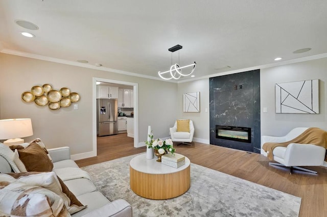 living room featuring a premium fireplace, an inviting chandelier, crown molding, and light hardwood / wood-style flooring