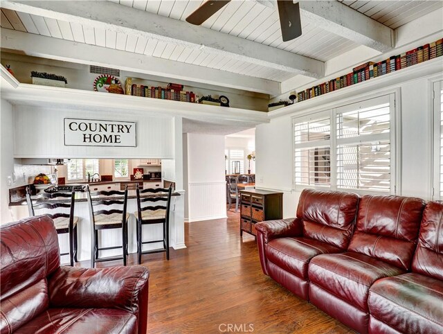 living room with ceiling fan, a wealth of natural light, dark wood-type flooring, and beamed ceiling