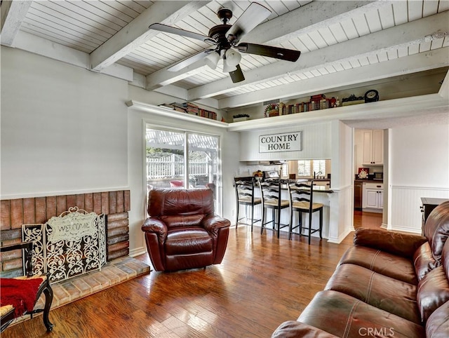 living room with a ceiling fan, wainscoting, wood ceiling, beamed ceiling, and wood finished floors