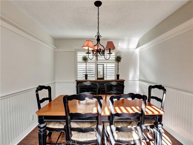 dining space featuring dark wood-type flooring, a notable chandelier, and a textured ceiling