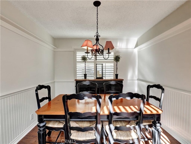 dining area featuring a textured ceiling, wainscoting, dark wood finished floors, and a notable chandelier