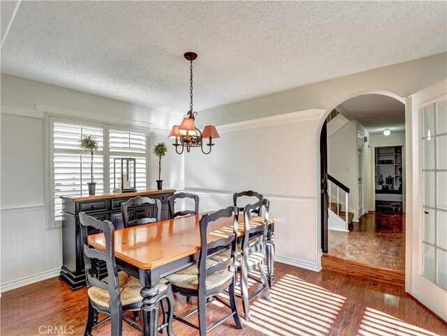 dining space featuring a textured ceiling, dark wood-type flooring, and a notable chandelier