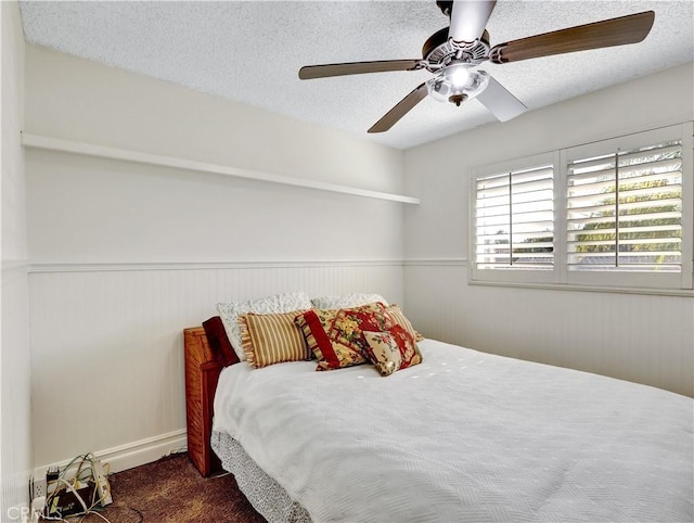 bedroom with a textured ceiling, ceiling fan, a wainscoted wall, and carpet