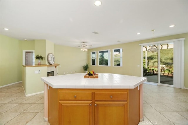 kitchen featuring a tiled fireplace, tile counters, ceiling fan, and a kitchen island