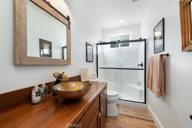 bathroom featuring vanity, hardwood / wood-style flooring, a shower with shower door, and toilet