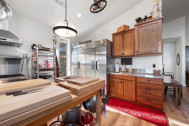 kitchen featuring vaulted ceiling, sink, hanging light fixtures, stainless steel counters, and light hardwood / wood-style flooring