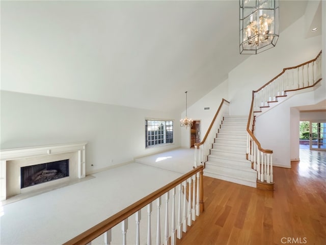 staircase featuring a chandelier, wood finished floors, high vaulted ceiling, and a high end fireplace