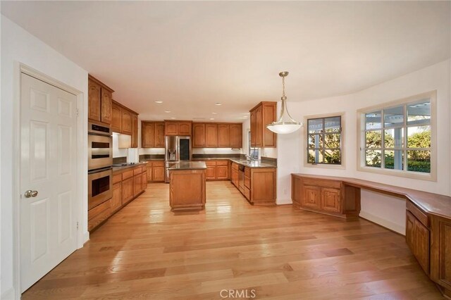 kitchen featuring pendant lighting, appliances with stainless steel finishes, light wood-type flooring, a center island, and built in desk