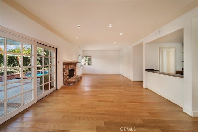 unfurnished living room featuring visible vents, crown molding, baseboards, a fireplace, and light wood-style floors