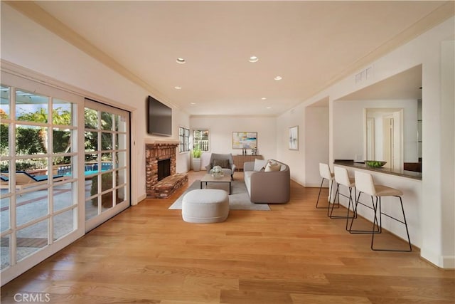 living area featuring light wood finished floors, visible vents, a brick fireplace, ornamental molding, and recessed lighting