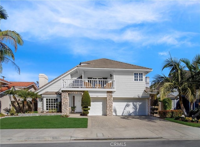 view of front of property featuring a front lawn, concrete driveway, a garage, a balcony, and stone siding