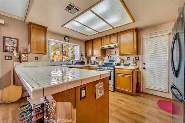 kitchen with tile countertops, light hardwood / wood-style flooring, kitchen peninsula, and stainless steel range with gas stovetop