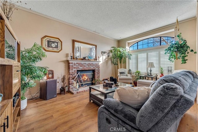 living room with light wood-type flooring, a brick fireplace, a textured ceiling, and ornamental molding