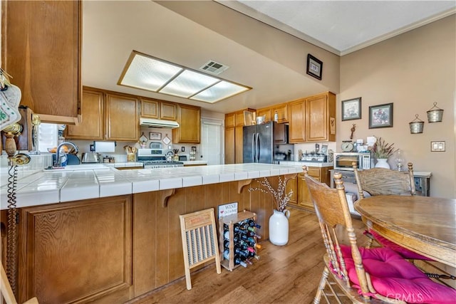 kitchen featuring tile counters, black refrigerator, light hardwood / wood-style floors, stainless steel stove, and kitchen peninsula