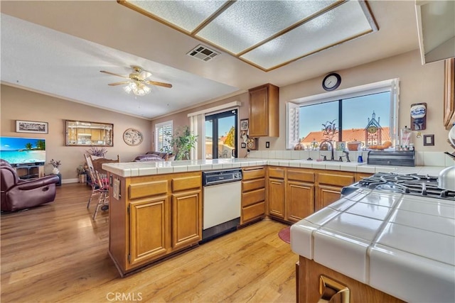 kitchen featuring light hardwood / wood-style floors, kitchen peninsula, tile counters, dishwasher, and sink