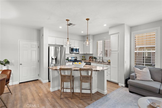 kitchen with appliances with stainless steel finishes, a kitchen island, pendant lighting, white cabinets, and sink