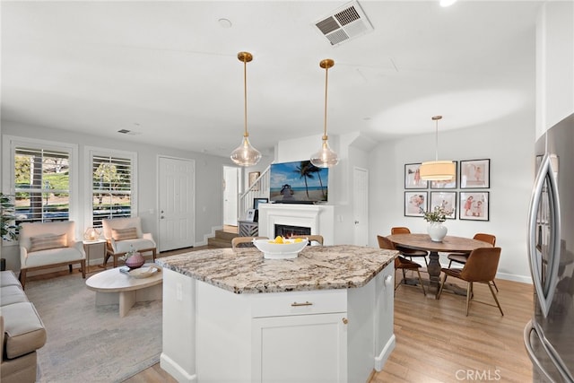 kitchen featuring decorative light fixtures, light stone countertops, white cabinets, and stainless steel refrigerator