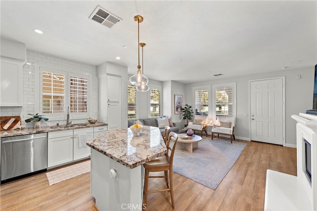 kitchen featuring a kitchen island, decorative light fixtures, white cabinetry, sink, and stainless steel dishwasher