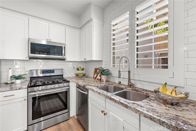 kitchen featuring stainless steel appliances, white cabinetry, light stone counters, and sink