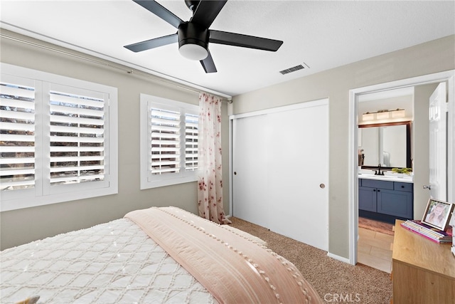 carpeted bedroom with ceiling fan, ensuite bathroom, a closet, and sink