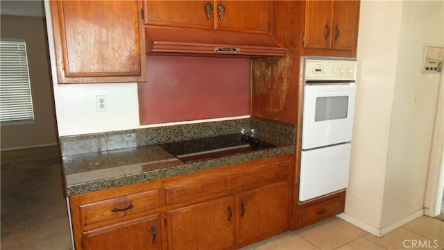 kitchen featuring light tile patterned floors, extractor fan, black stovetop, and dark stone countertops