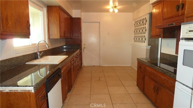 kitchen with white appliances, light tile patterned floors, dark stone countertops, and sink