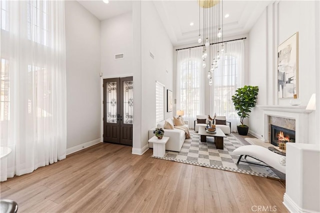 living area with an inviting chandelier, a high ceiling, light wood-type flooring, a fireplace, and french doors