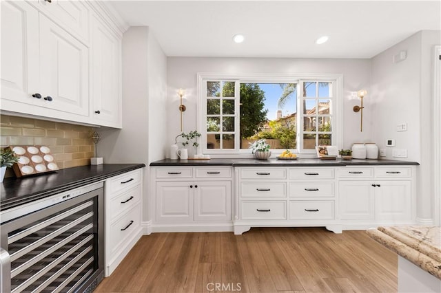 kitchen with white cabinets, dark stone countertops, tasteful backsplash, wine cooler, and light wood-type flooring