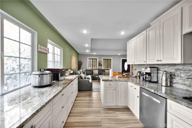 kitchen with kitchen peninsula, dishwasher, light stone counters, and white cabinetry