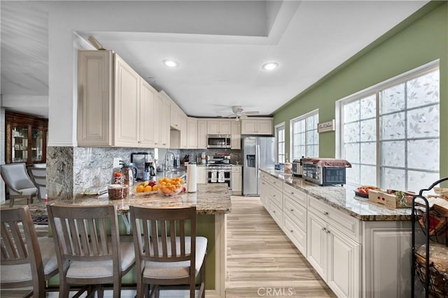 kitchen featuring appliances with stainless steel finishes, tasteful backsplash, a kitchen breakfast bar, light stone countertops, and light hardwood / wood-style flooring