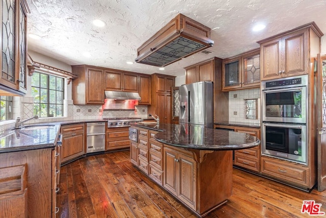 kitchen featuring dark wood-type flooring, a center island, stainless steel appliances, and dark stone countertops