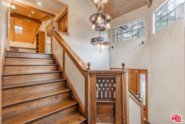 staircase with beam ceiling, a high ceiling, wood ceiling, and an inviting chandelier