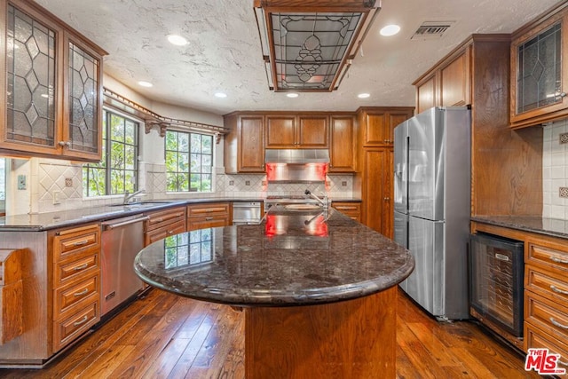 kitchen with beverage cooler, appliances with stainless steel finishes, extractor fan, a kitchen island, and dark wood-type flooring